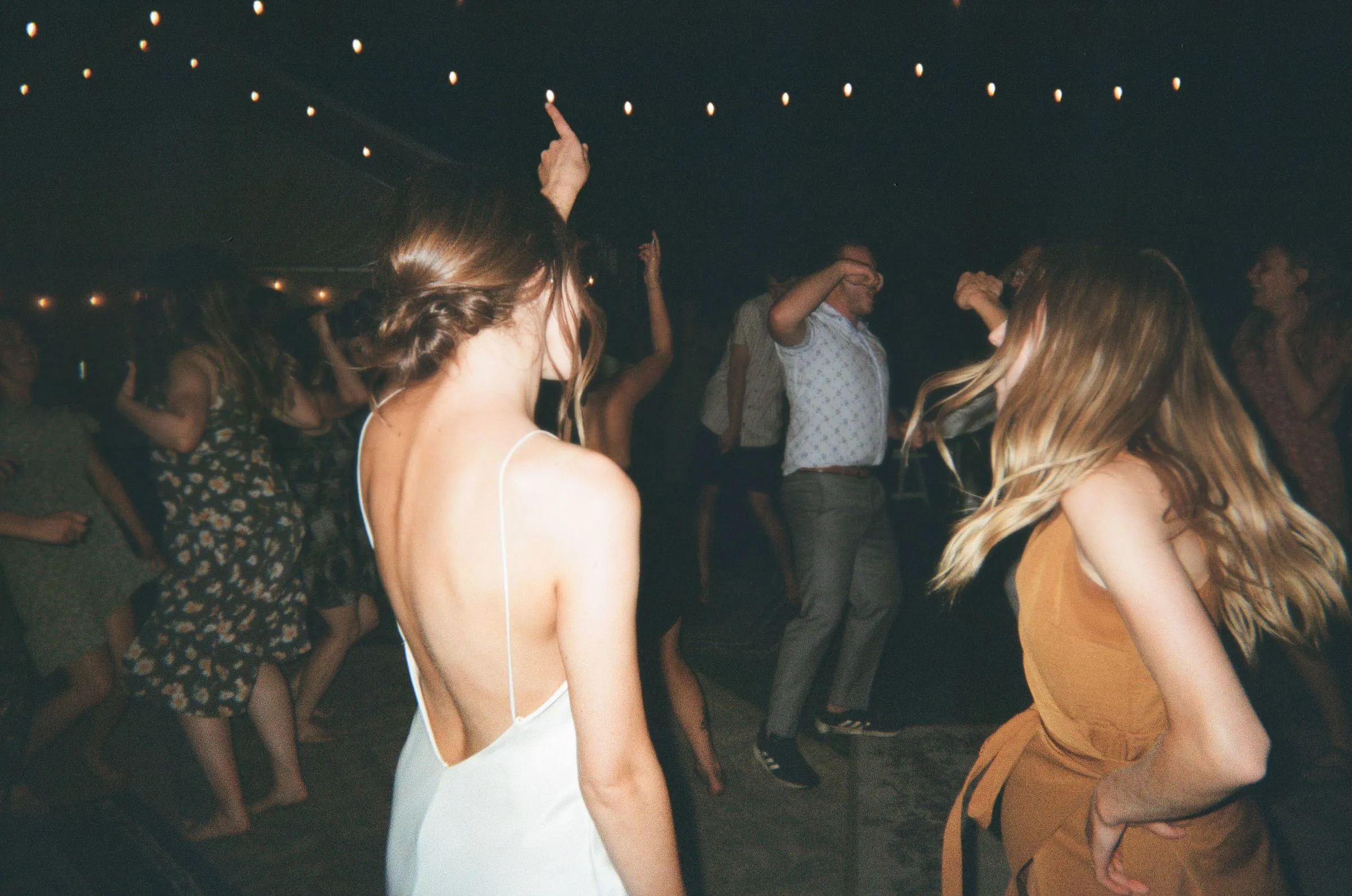 Guests dance in the dark under string lights, the bride seen from behind with her arm raised