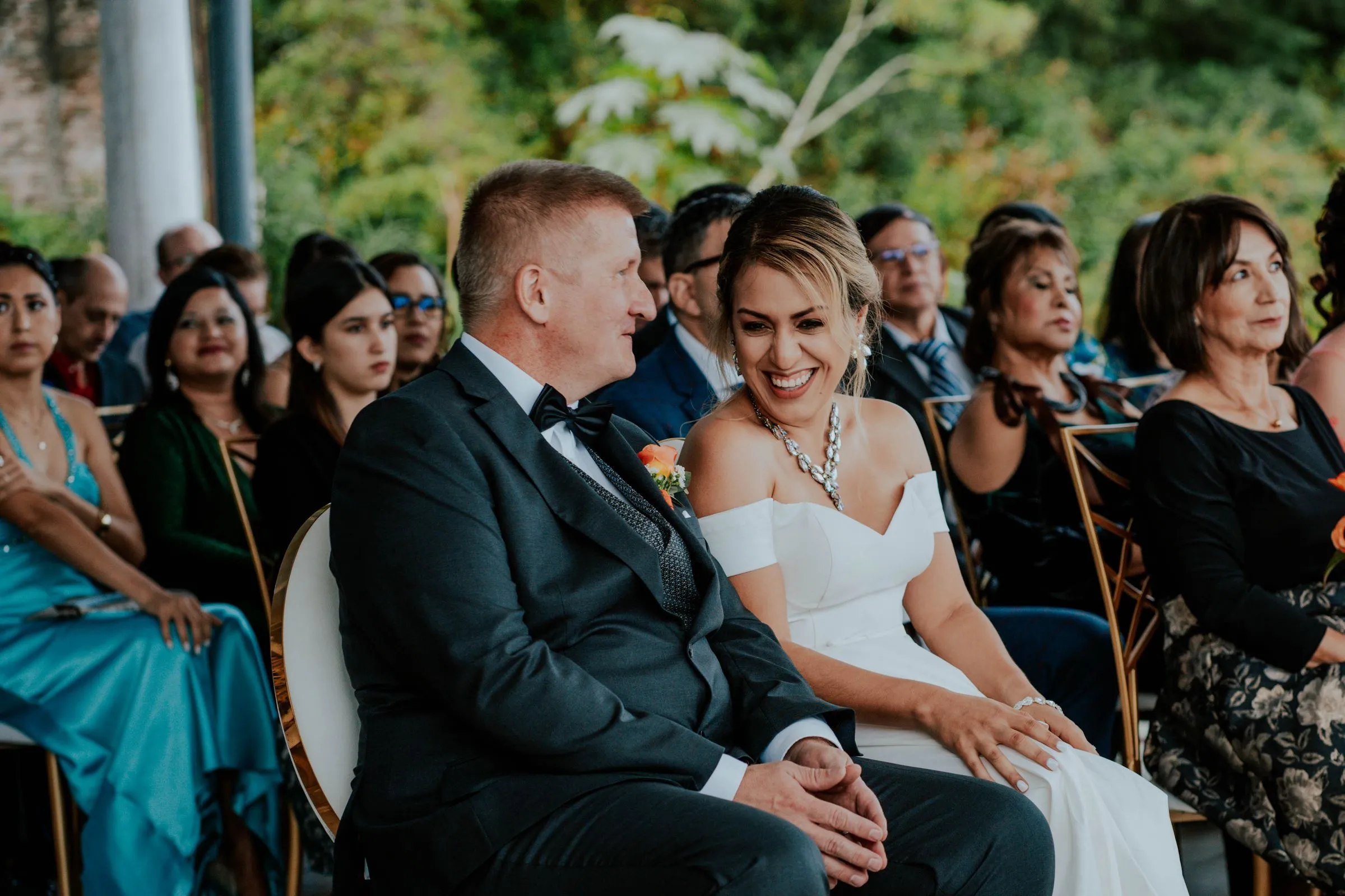 The couple sit in the front row among their guests, both laughing