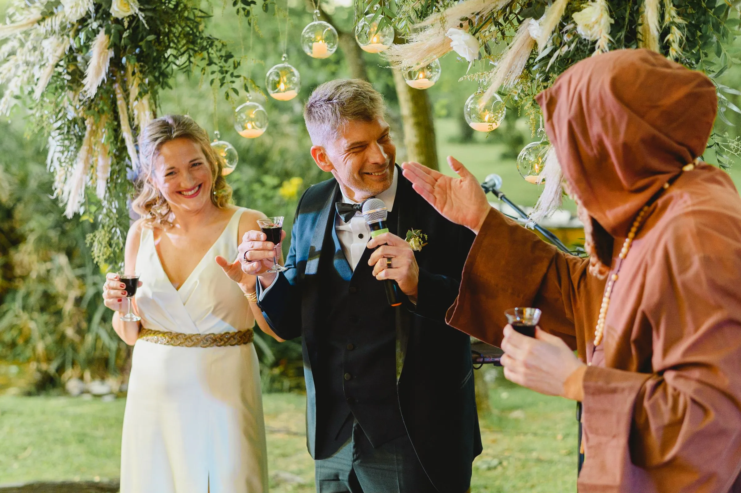 The couple raise their glasses with a guest in a garden hung with glass lanterns